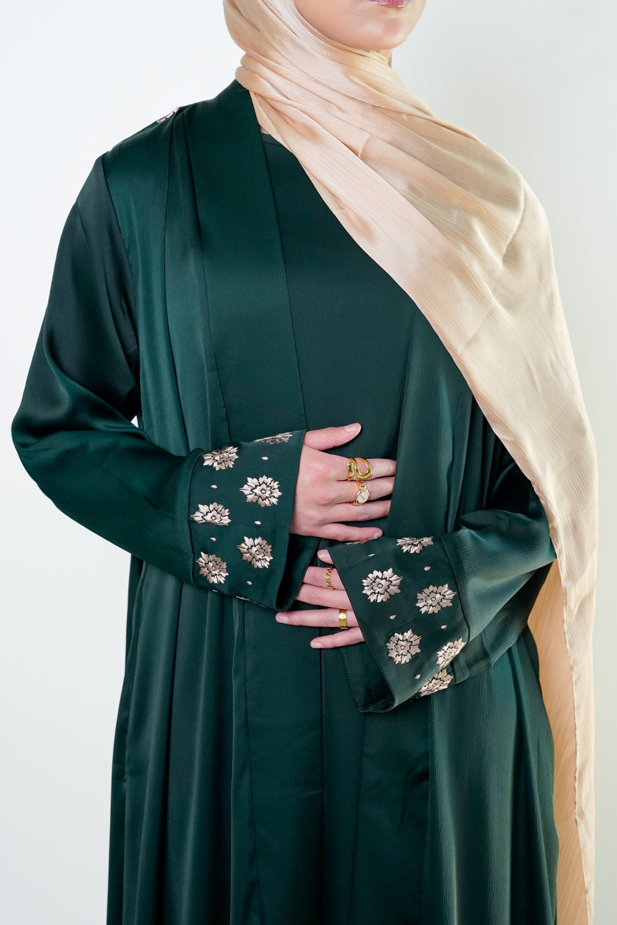 The image shows a close-up of a woman wearing an elegant emerald green kimono with intricate floral embroidery on the cuffs.