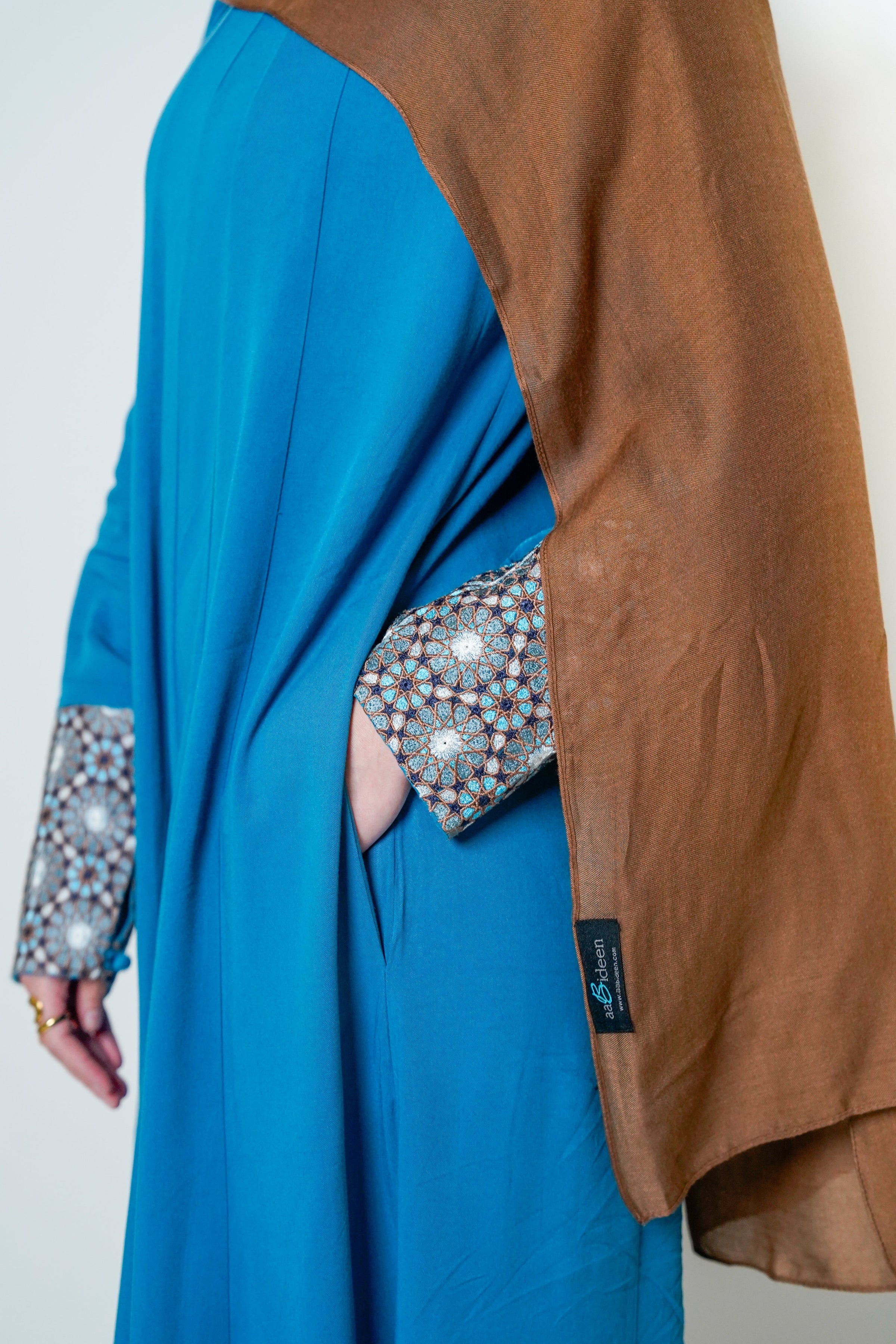 Side view of the Luxury Caspian Blue Embroidered Cuff Abaya, highlighting the intricate cuff embroidery in blue and gold with side pockets. The abaya is made from soft fabric with a flowing design, offering both sophistication and comfort.