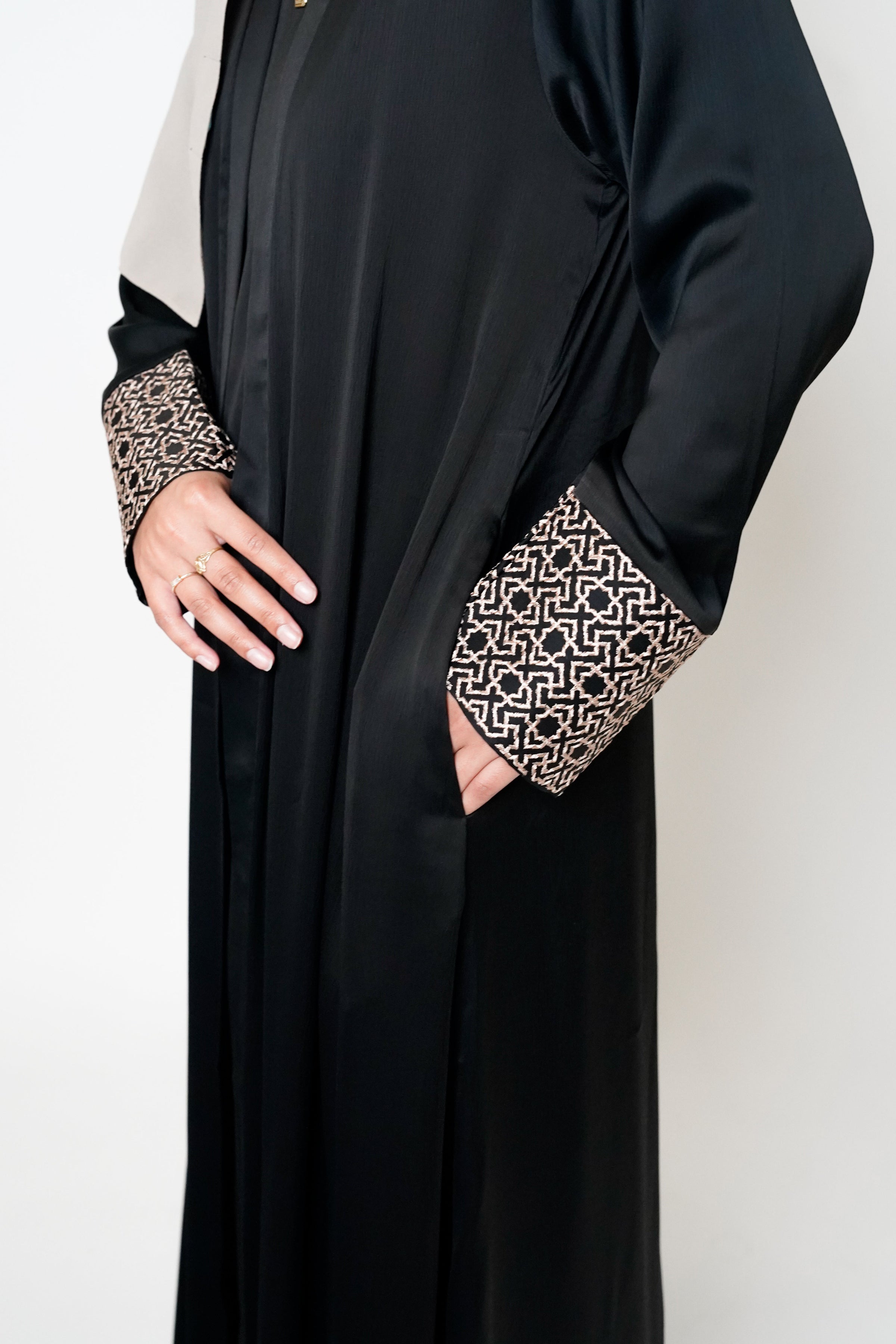 Close-up of the black abaya featuring intricate geometric embroidery with side pockets in beige on the cuffs, adding sophistication and style to the elegant design.