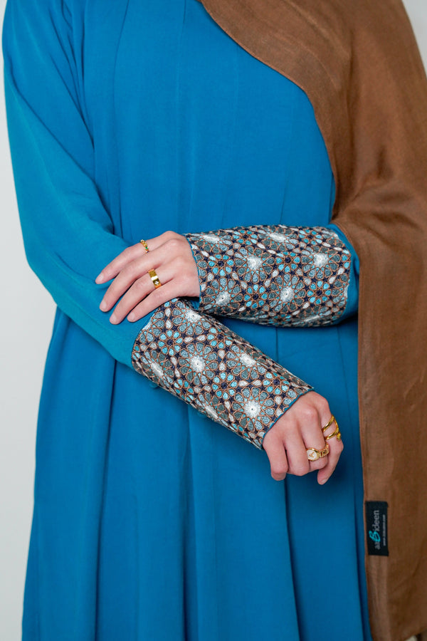 Close-up of the Luxury Caspian Blue Embroidered Cuff Abaya, showcasing intricate cuff embroidery in vibrant blue and gold. The abaya is made from soft fabric with panels for a full, flowing design, offering both comfort and sophistication.