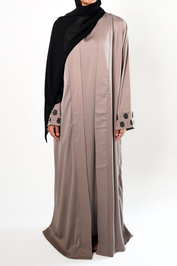 A woman wearing a sand embroidered black kimono with black floral embroidery on the cuffs, paired with a black hijab